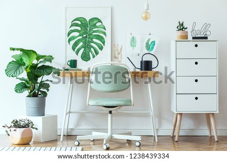 Stylish scandinavian home office desk with mock up poster frames, a lot of plants and office accessories. Brown wooden parquet and white backgrounds wall. Modern composition of homeoffice desk.