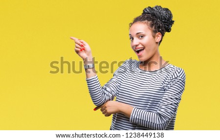 Young braided hair african american girl wearing sweater over isolated background with a big smile on face, pointing with hand and finger to the side looking at the camera.