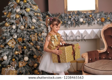 a girl in a dress with gold donuts is standing near the New Year tree with presents and laughing