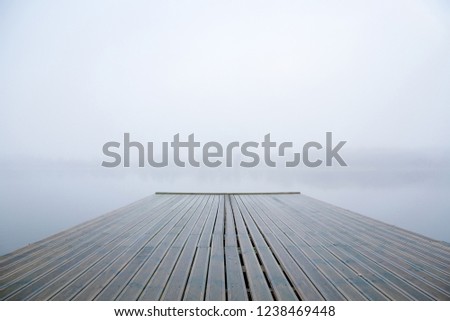 Wooden footbridge on lake. Mist over water. Foggy air. Early chilly morning in late autumn. Peaceful atmosphere in nature. Empty place for text, quote or sayings.