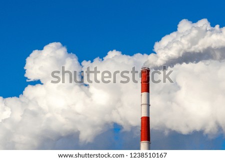 Smoking pipe of a power plant against the backdrop of a clear blue sky.