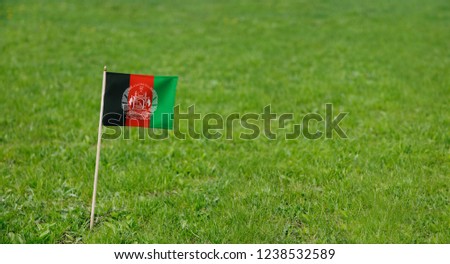 Afghanistan flag. Photo of Afghanistan flag on a green grass lawn background. Close up of national flag waving outdoors.