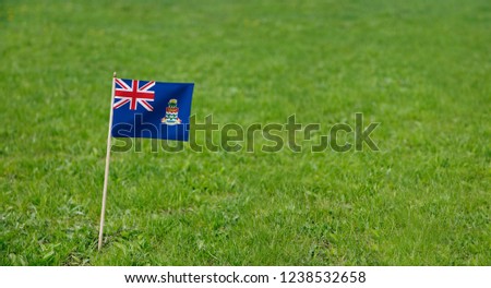 Cayman Islands flag. Photo of Cayman Islands flag on a green grass lawn background. Close up of national flag waving outdoors.