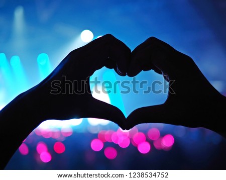 K-Pop music theme or Live concert background with silhouette hands of audience making heart shaped hand gesture for artist supporting on blurred background of a large stage with bokeh defocused lights