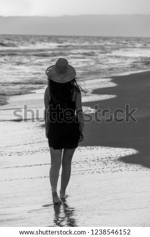 The young woman with hat walking in beach at sunset. Black and white background.
