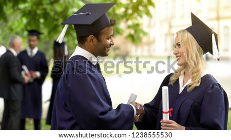 Students in graduation gown with diplomas talking, shaking hands and hugging