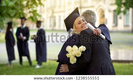 Father hugging his graduate daughter giving flowers, congratulating, paternity Royalty-Free Stock Photo #1238555551
