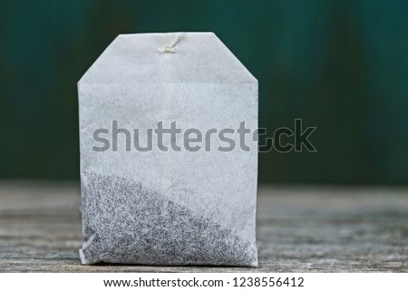 white tea bag with black tea on a gray table on a green background