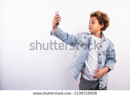 Cool african american boy talking on the phone, chatting and making selfie. Kids and gadgets. Modern children. New pics on white background. Shooting in November 2018. 
