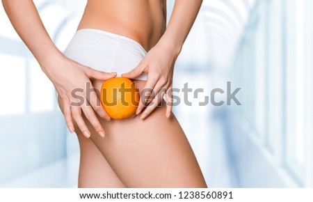 Female slender body in sport underwear holding orange on blurred background