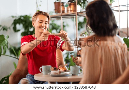 people, technology and lifestyle concept - female friends drinking tea and photographing food by smartphone