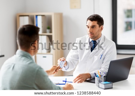 medicine, healthcare and people concept - doctor giving pills to male patient at medical office in hospital Royalty-Free Stock Photo #1238588440