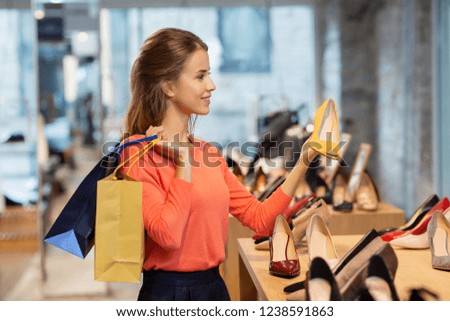 sale, fashion and people concept - happy young woman with shopping bags choosing shoes at store Royalty-Free Stock Photo #1238591863
