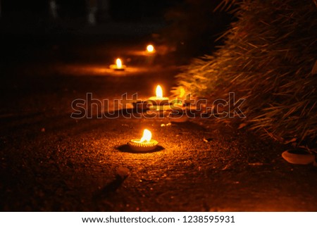 Burning candle on the ground in darkness with grain effect. Candle light in clay pot at night during Loy Krathong festival in Chiang Mai, Thailand. Beautiful abstract background.
