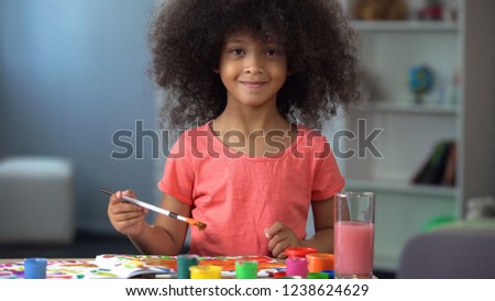 Nice African female kid painting a picture and smiling into camera, childhood