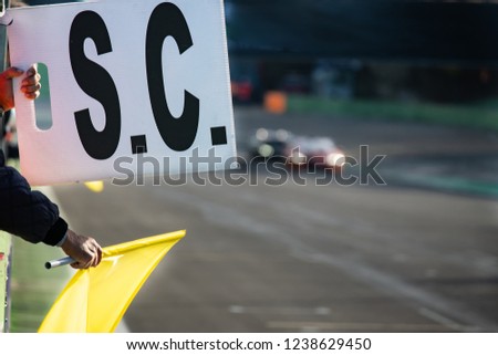 Danger on track warning waved yellow flag and safety car sign exposed during car racing, selective focus