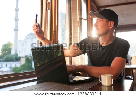 A young blogger records video or communicates with subscribers online while sitting at a laptop. In the background is the Blue Mosque in Istanbul in Turkey.