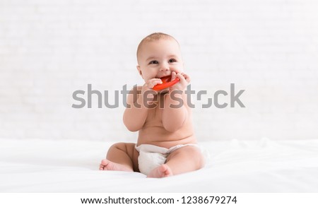 Infant growing first tooth. Cute newborn baby biting teether in bed, copy space Royalty-Free Stock Photo #1238679274