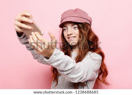  cheerful little girl with curly hair l taking a selfie isolated over pink background