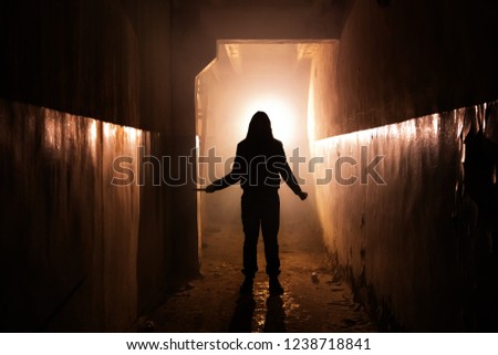 Creepy silhouette of unknown man with knife in dark corridor of abandoned building. Horror about maniac concept