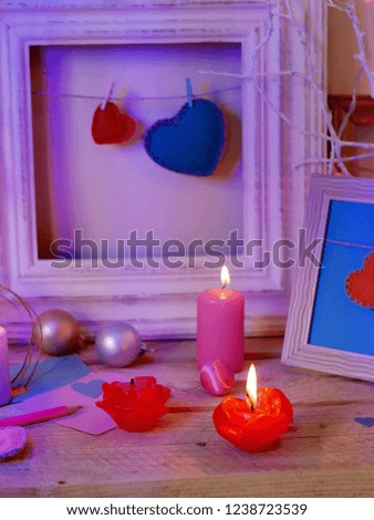 Seasonal festive interior composition of lit candles, decor, wooden frames, decorative lamps, felt hearts, paper for notes on a wooden table, the concept of congratulations on the holiday, a romantic 