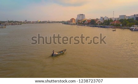 AERIAL: Flying along local person navigating a wooden boat across the calm river on a breathtaking tropical evening. Unknown person crossing the delta to go to the Vietnamese city at golden sunrise.