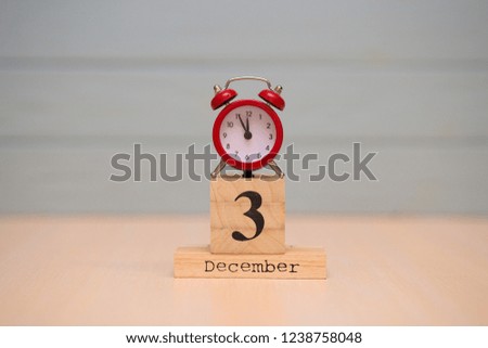 December 3rd set on wooden calendar and red alarm clock with blue background. Clock showing five minutes to midnight