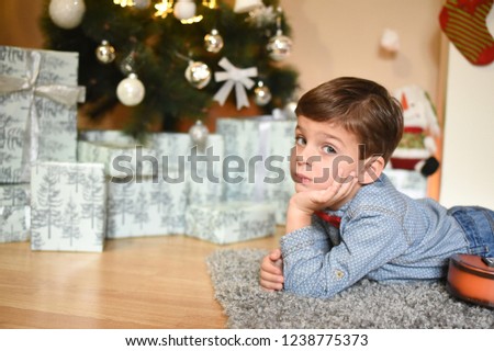 Boy wait a New Year. Happy boy with a guitar sit under a Christmas tree