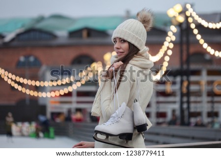 Charming young woman in the Park near the ice rink. Happy young woman in knitted sweater and hat is going skating