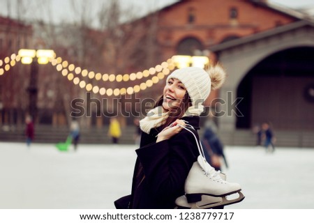 Charming young woman in the Park near the ice rink. Smiling brunette with skates, winter leisure and relaxation