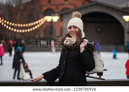 Charming young woman in the Park near the ice rink. Happy brunette with skates, winter leisure and relaxation