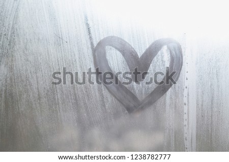 A heart-shaped drawing drawn by a finger on a misted glass in rainy weather