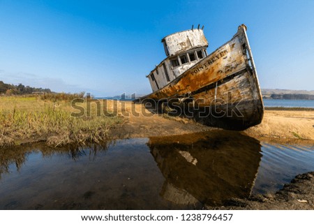 A wrecked rusty ship lays on a sand bank and reflects in the water