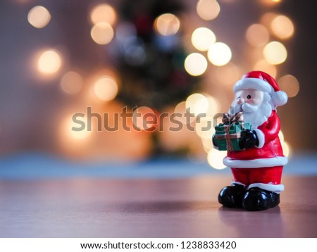 Santa claus holding a gift box standing in front of the christmas tree with lighting decoration, blur background