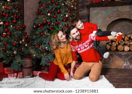 Young family: father, mother and son in warm red sweaters doing selfie by red smartphone with decorated christmas tree near fireplace during winter holidays. Merry Christmas and Happy New Year concept