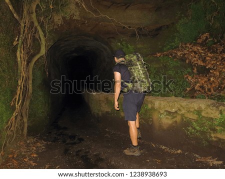 Picture from night hiking. Tourist looking in the dark tunnel on the levada trail. Hiker on the evening path with tunnel  and tree.