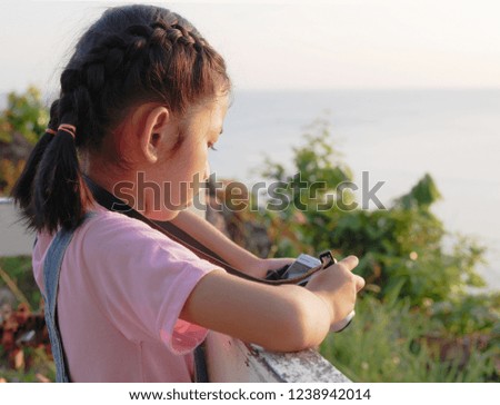 A little girl holding camera with taking a picture. Asian kid making photo in twilight with copy space.