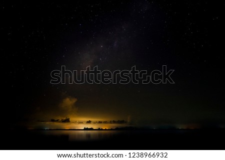 Stardust in dark night with noise and grain on the sky with cloud and light of city on bottom.