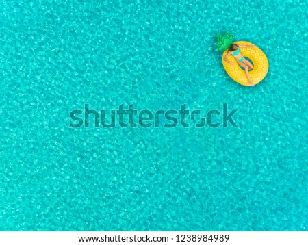 Aerial view of girl floating on inflatable pineapple mattress on transparent sea.