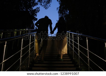 Young women and men are going the upstairs and hold hands. Picture of strong union and family. Silhouettes loving couple are walking up the stairs. Symbol of strong love.