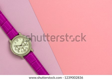 Women's fashion wrist watch with purple strap. Watch lying on purple paper, also close to a large pink sheet of paper. Close up