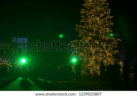 Silhouettes of people enjoying winter holidays atmosphere outdoor near tall illuminated Christmas tree in the night.