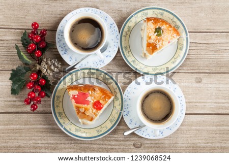 Two cut pieces of Spanish typical dessert of epiphany  and two cups of coffe, pine cone and mistletoe on wood  background from above 