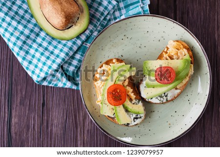 Toasts with avocado pieces, cherry tomatoes, scrambled eggs and soft cream cheese.
