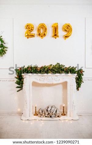 Christmas room with decorated white fireplace with gifts and garlands. Balloons numbers New year 2019. Place for text. Amber lights around.