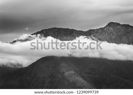 Low hanging white clouds in front of a mountain with dark moody sky