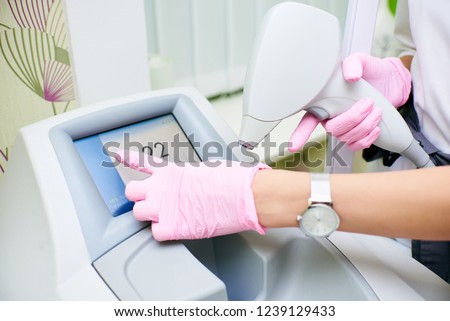 Hands of the doctor in pink gloves hold the device for an epilation and press the touch screen. The concept of control device, laser hair removal Royalty-Free Stock Photo #1239129433