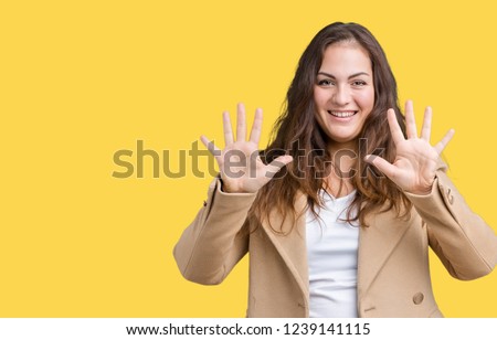 Beautiful plus size young woman wearing winter coat over isolated background showing and pointing up with fingers number ten while smiling confident and happy.