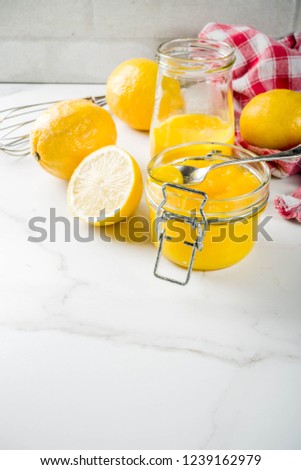 Homemade lemon curd in glass jars with fresh lemons, white marble background copy space