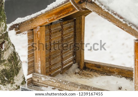 A wooden manger in winter for birds hanging on a tree branch.